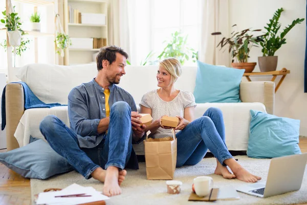 Szczęśliwa para siedzi na podłodze w domu, jedząc hamburgery. — Zdjęcie stockowe