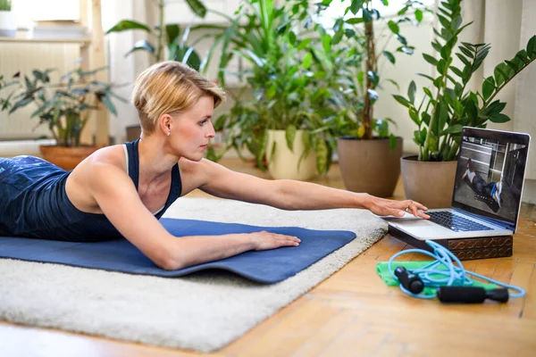 Visão lateral da jovem fazendo exercício dentro de casa, seguindo vlogger . — Fotografia de Stock