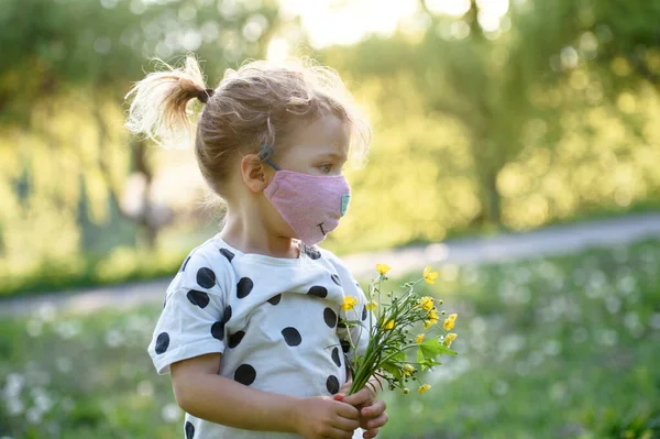 Menina pequena com máscara facial em pé ao ar livre, conceito coronavírus . — Fotografia de Stock
