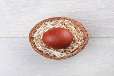 Oval sepette tek bir kahverengi benekli yumurta ve ahşap arka planda saman eşmerkezli halkalar.