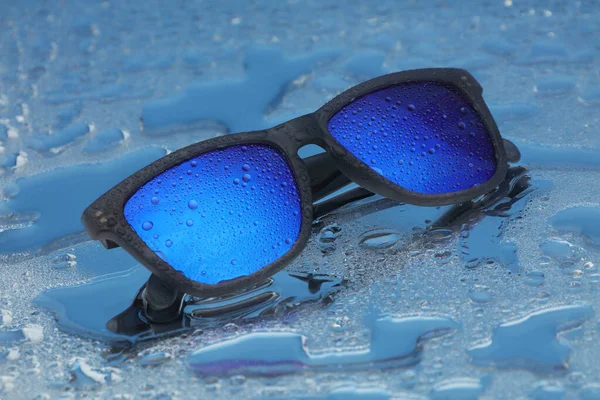 Blue sunglasses with water drops on water reflection — Stock Photo, Image