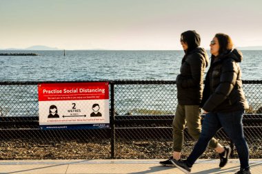 White Rock, Kanada - 25 Mart 2020: Covid-19 sosyal mesafe işaretini geçen iki yaya