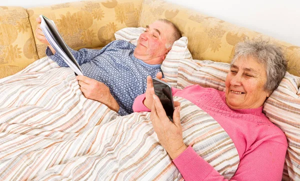 Hombre mayor leyendo y su esposa navegando por Internet — Foto de Stock