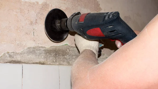 Grinding the walls with a drill and an emery wheel.The man grinds the concrete wall.