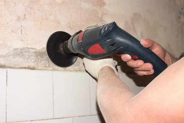 Grinding the walls with a drill and an emery wheel.The man grinds the concrete wall.