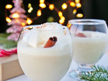Gözlüklü eggnog ve masada hediye, arka planda Noel ışıkları.