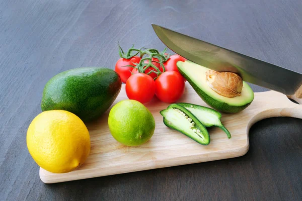 Guacamole avocado spread ingredients on wooden board over dark background. — Stock Photo, Image