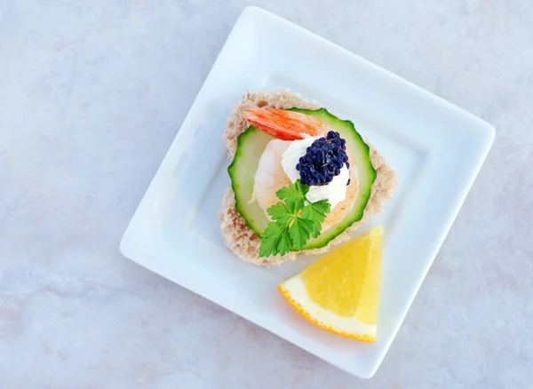 Élégantes canapés aux crevettes et au caviar noir servis dans un plat de service en porcelaine blanche sur plateau marbré, vue sur le dessus — Photo