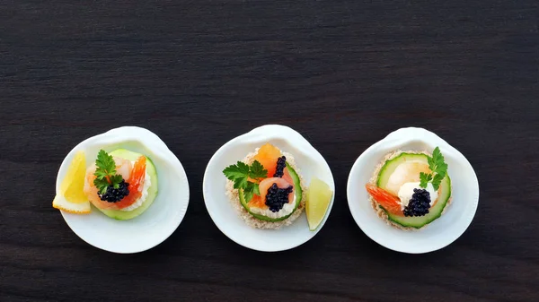 Eleganti tartine con salmone affumicato, gamberetti e caviale nero in piatto di porcellana a forma di guscio singolo da servire su tavolo di legno scuro — Foto Stock