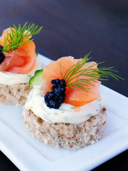 Comida para dedos con salmón ahumado y caviar en bandeja blanca sobre fondo oscuro —  Fotos de Stock