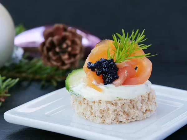 Nourriture savoureuse aux doigts avec saumon fumé et caviar sur plateau blanc sur fond sombre Photo De Stock