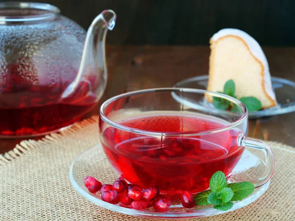 Beker van granaatappel thee met munt en thee pot met een stuk taart over jute op donkere achtergrond — Stockfoto