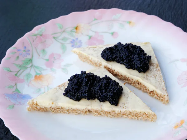 검은 슬레이트 접시 위의 다채 로운 판위에 놓인 빵 조각 위의 검은 캐비어 — 스톡 사진