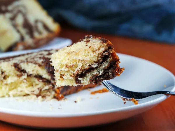 Bite of chocolate marble cake on fork over white plate — Stock Photo, Image
