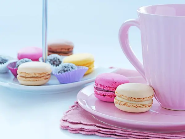 Frühstück mit französischen Macarons und einer Tasse Kakao in rosa Porzellanbecher. Auswahl kleiner Kekse in einem Keksfach im Hintergrund — Stockfoto