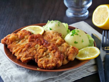 Limon dilimleri ve maydanoz yapraklarıyla servis edilen patates salatalı sosis şnitzel.