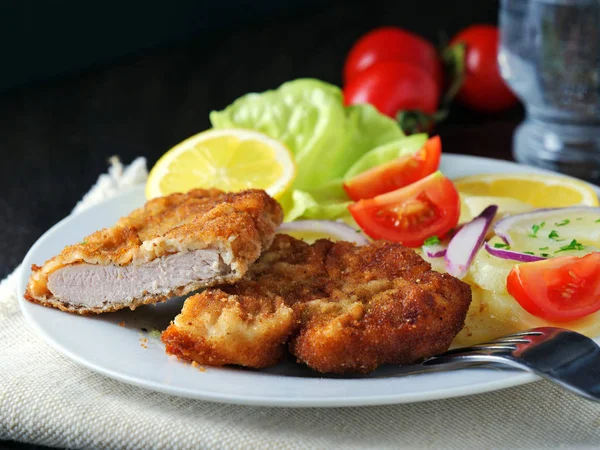 Wiener Schnitzel met aardappelsalade geserveerd met citroenschijfjes en peterseliebladeren Stockfoto