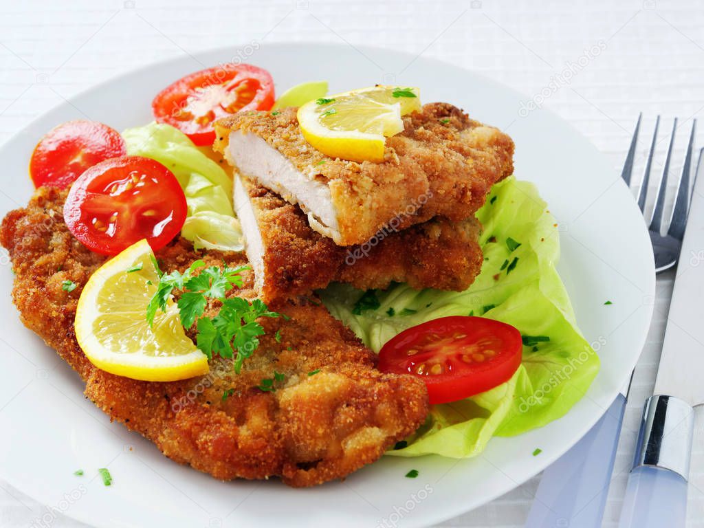 Wiener Schnitzel with potato salad served with lemon slices and parsley leaves