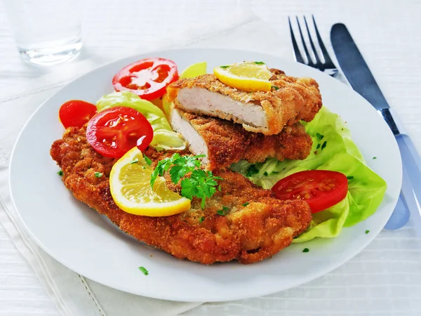 Schnitzel salchicha sobre hojas de lechuga con tomates en rodajas y limón en plato blanco — Foto de Stock