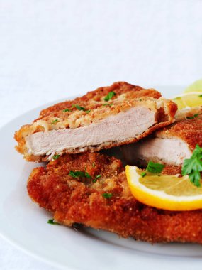 Sosis Schnitzel limon dilimleri ve maydanoz yapraklarıyla servis edilen beyaz, dikey...