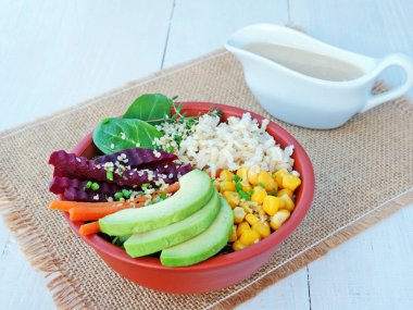 Kahverengi pirinç, kırmızı lahana, avokado, havuç, ıspanak ve tahin soslu pancar kökü ile servis edilen kase tabağı.