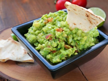 Avokado sosu, tahtadan tahta kesme tahtasının üzerinde, siyah kare kaseye batırılmış. Meksika guacamole sosu..