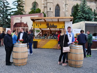 İnsanlar 19 Mayıs 2018 'de Romanya' nın Cluj-Napoca kentindeki çok sayıda yiyecek ve şarap standının önünde fıçı masalarında içki içiyorlar.
