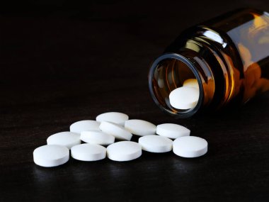 Beyaz yuvarlak haplar açık kahverengi bir şişeden dökülüyor.