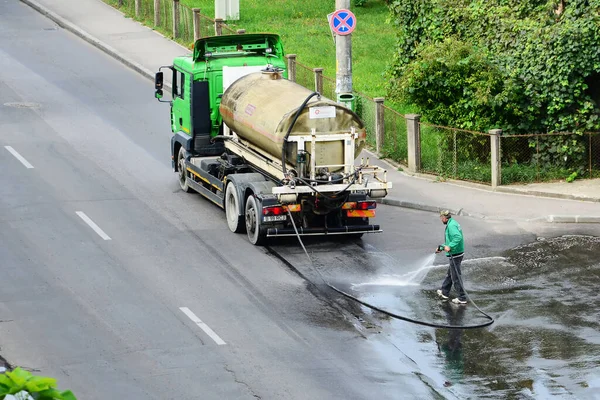 2014年8月26日 一名公用事业工人在罗马尼亚克洛伊纳斯卡用连接蓄水池卡车的软管清洗和消毒街上的沥青 — 图库照片