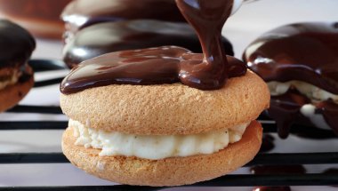 Çikolatalı ganache 'yi vanilya kremalı sandviç kurabiyelerinin üzerine döküyorum.