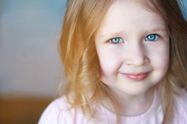 Mavi gözlü ve gülümseyen sarı saçlı küçük kız.
