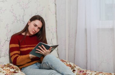 Evde karantinaya alınmış bir kız yatakta kitap okuyor.