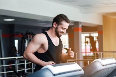 Genç bir adam koşu bandında koşuyor ve gülümsüyor.