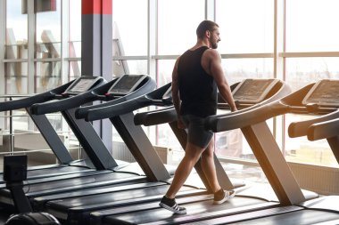 Spor salonunda koşu bandında koşan bir gencin tam boy profili.