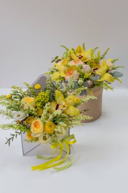 Açık arkaplanda bej bir şapka kutusunda taze çiçeklerin (gül, orkide, şakayık, okaliptüs) kompozisyonu