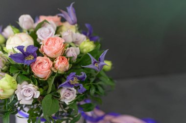 Koyu gri arkaplan üzerinde renkli kurdeleler bulunan yuvarlak bir kutuda parlak çiçek aranjmanı (renk: mor, pembe, yeşil. Çiçekler: gül, şakayık)