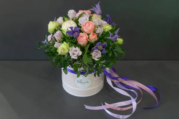 bright floral arrangement in a round box with colored ribbons on a dark gray background (color: purple, pink, green. Flowers: rose, peony)