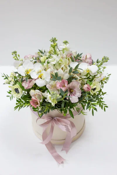 华丽的花朵布置在一个圆形的帽盒中 有缎带和浅色背景 仙人掌 金银花 开心果叶 免版税图库照片