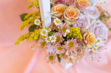 Hassas bir çiçek aranjmanı ve pembe arka planda bir kalem (Renkler: sarı, pembe, beyaz, pembe, vanilya. Çiçekler: gül, karanfil, solidaga, kasımpatı)