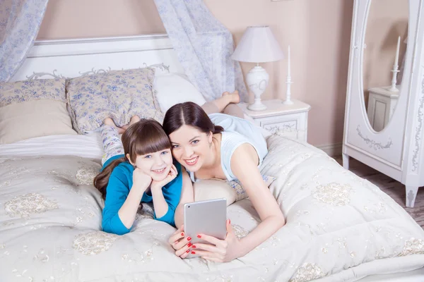 Feliz madre e hija yacían en la cama con la tableta digital . — Foto de Stock