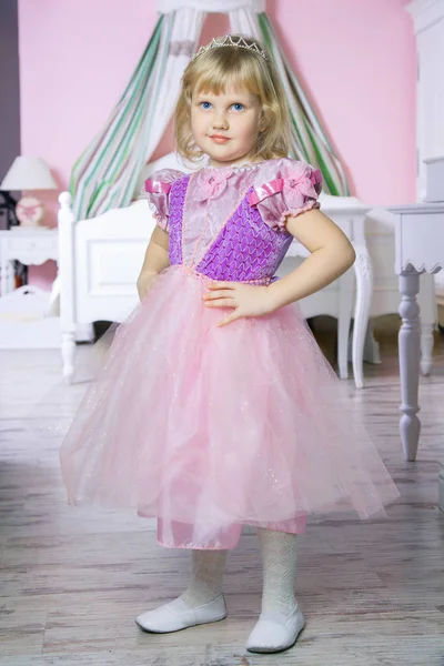 Ευτυχισμένη πριγκίπισσα κοριτσάκι σε ροζ φόρεμα και στέμμα στο δωμάτιό της Βασιλικής θέτοντας και χαμογελαστός. — Φωτογραφία Αρχείου