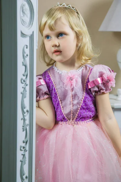 Ευτυχισμένη πριγκίπισσα κοριτσάκι σε ροζ φόρεμα και στέμμα στο δωμάτιό της Βασιλικής θέτοντας και χαμογελαστός. — Φωτογραφία Αρχείου