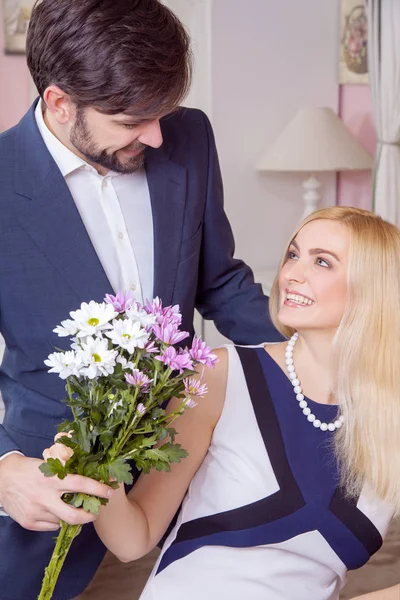 Joven hombre guapo sorprendiendo a su hermosa novia y le da un ramo de flores blancas púrpura . — Foto de Stock