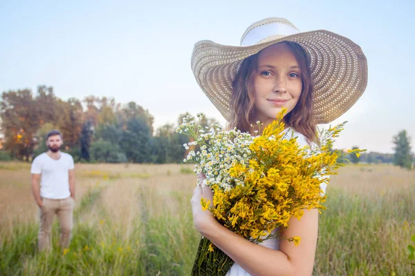 Buket sarı çiçek tutan ve kameraya sevgilisi ile arka plan üzerinde seyir güzel kadın. — Stok fotoğraf