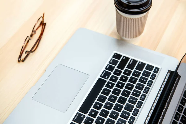 Schreibtisch mit Laptop, Brille und einer Tasse Kaffee. — Stockfoto