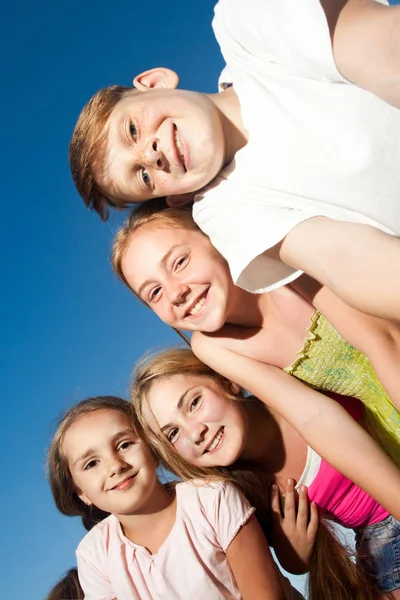 Cuatro niños hermosos felices mirando la cámara desde arriba en el soleado día de verano y el cielo azul. mirando a la cámara con cara divertida y sonrisa dentada . —  Fotos de Stock