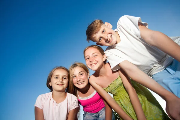 Cztery szczęśliwe dzieci piękne patrząc na kamery od góry w słoneczny letni dzień i błękitne niebo. patrząc na kamery z śmieszną twarz i Uśmiech zębiczny. Obrazy Stockowe bez tantiem