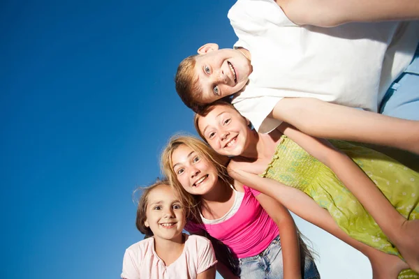 Cztery szczęśliwe dzieci piękne patrząc na kamery od góry w słoneczny letni dzień i błękitne niebo. patrząc na kamery z śmieszną twarz i Uśmiech zębiczny. Zdjęcie Stockowe