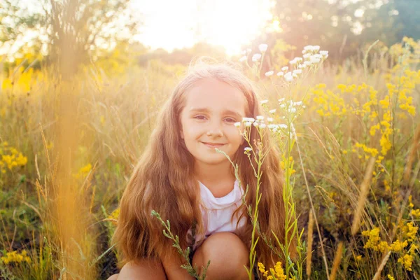Hermosa niña con el pelo largo y sonrisa en el verano en el parque de la puesta del sol. posando y mirando a la cámara y sonriendo . —  Fotos de Stock