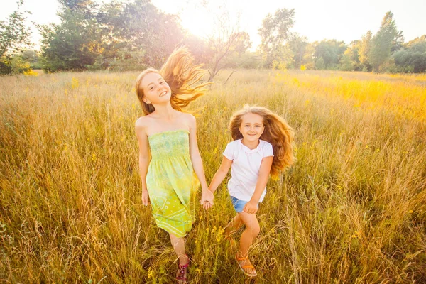 Dos hermosas hermanas corriendo en el césped en el parque natural al aire libre en el verano. Libertad y despreocupación. Feliz infancia. . —  Fotos de Stock